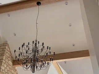 Black chandelier hanging beside an oak ceiling beam