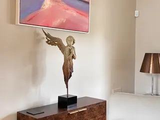 Bronze figure displayed on a console table beneath a painting